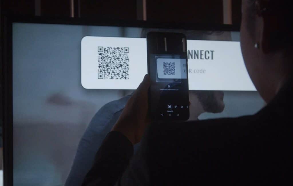 A person is holding a device scanning a QR code on a screen with the word "CONNECT" displayed above.