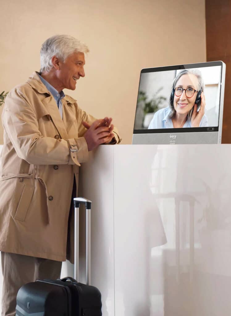 A VERA receptionist checks in an older man visiting a senior living community. The live receptionist is pictured on a screen, handling the check-in process from a remote location.