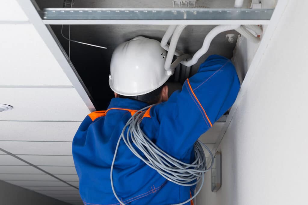foreman in blue uniform and white hard hat laying wiring in a hidden false ceiling system