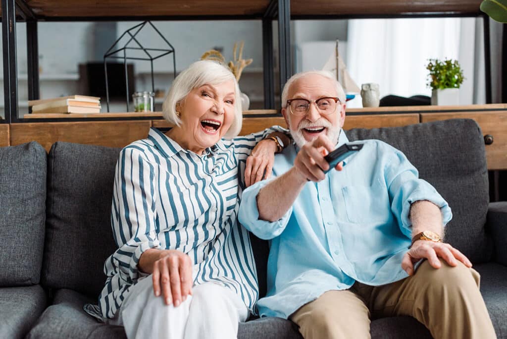 Senior couple laughing while watching tv on couch