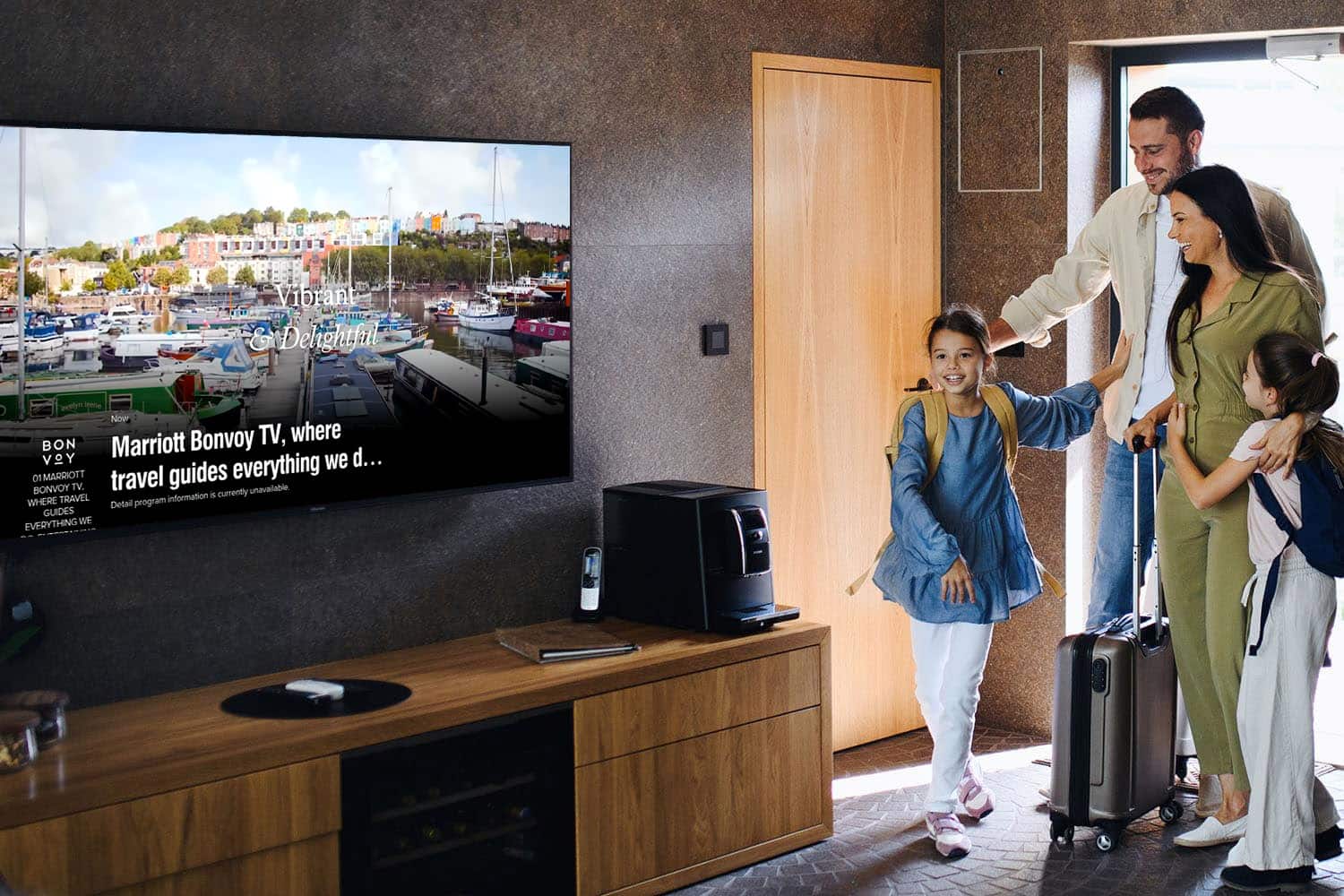 A family with two children entering a hotel room with a large TV screen displaying colorful marina imagery and text about Marriott Bonvoy TV.