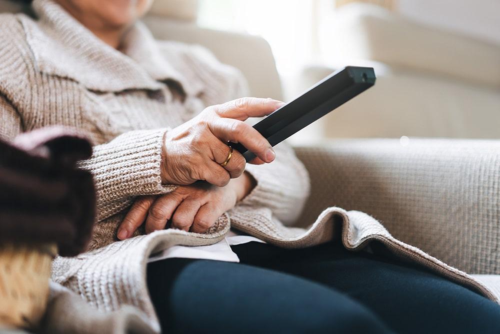 Elderly person uses TV remote control from a seated position.