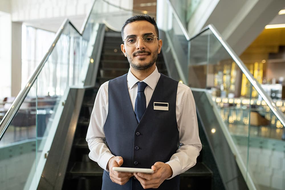 Young hotel manager with tablet standing in front of escalator